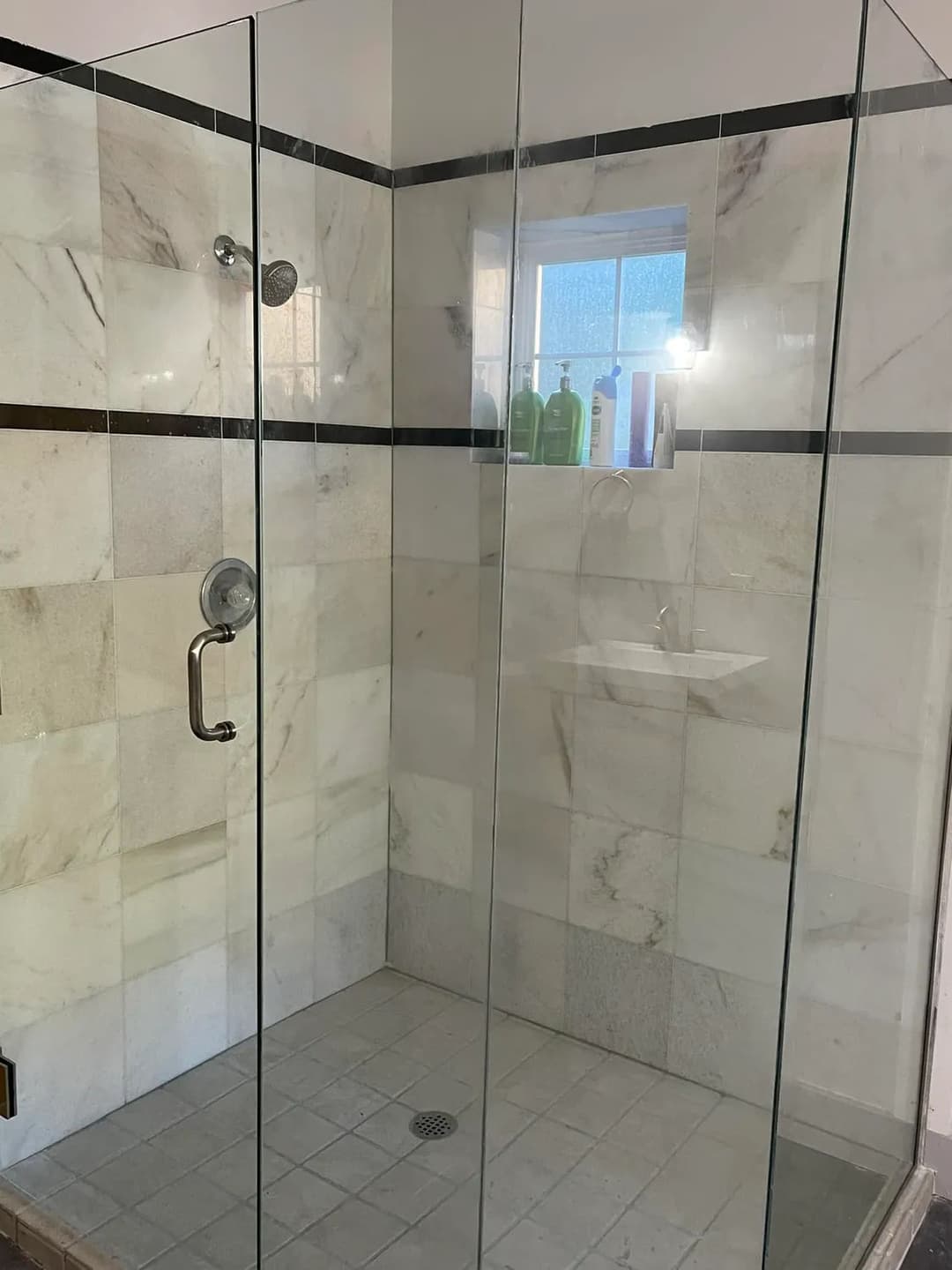Modern glass shower enclosure with marble tiles and minimalist design, featuring a built-in shelf.