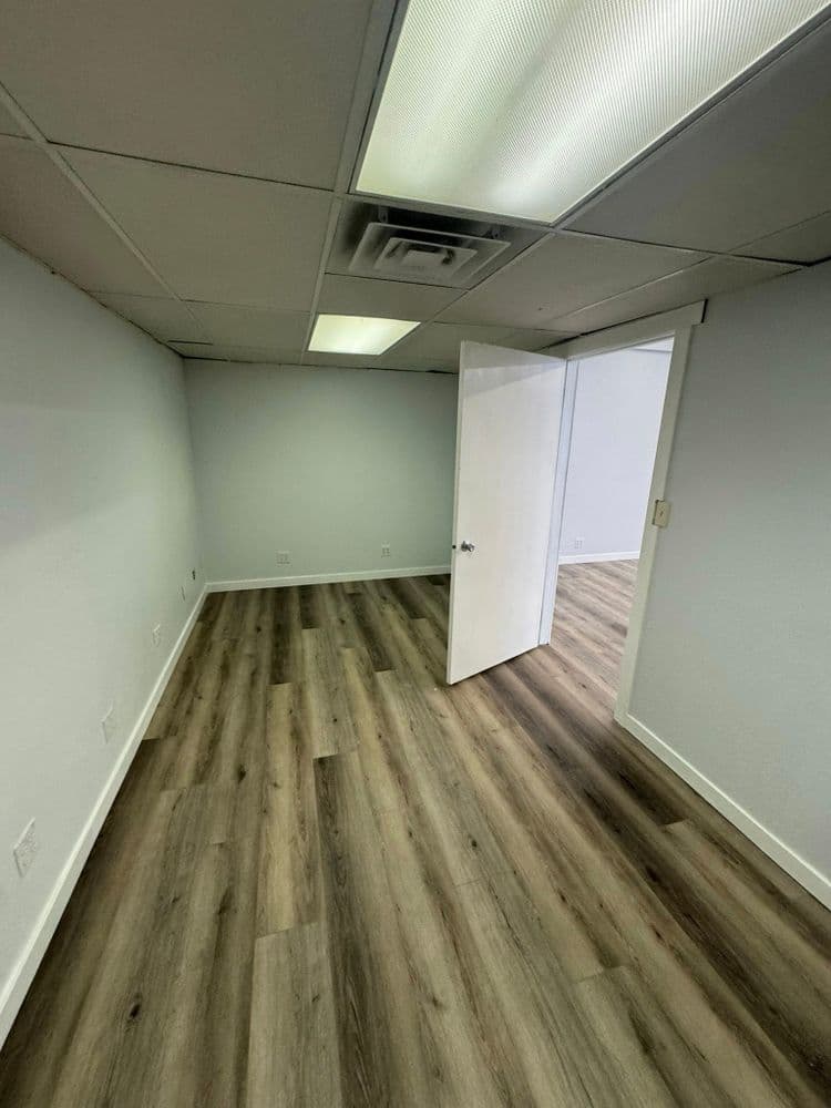Empty office space with open door, modern flooring, and neutral wall color. Ideal for leasing.