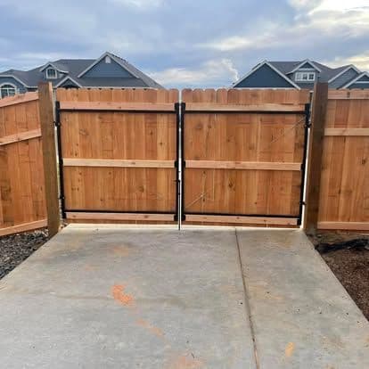 Wooden fence gate with metal latch, set against a suburban backdrop and cloudy sky.