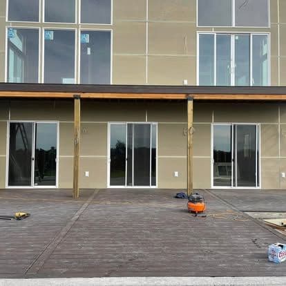 Modern home facade with large windows and a wooden deck under construction. Tools visible.