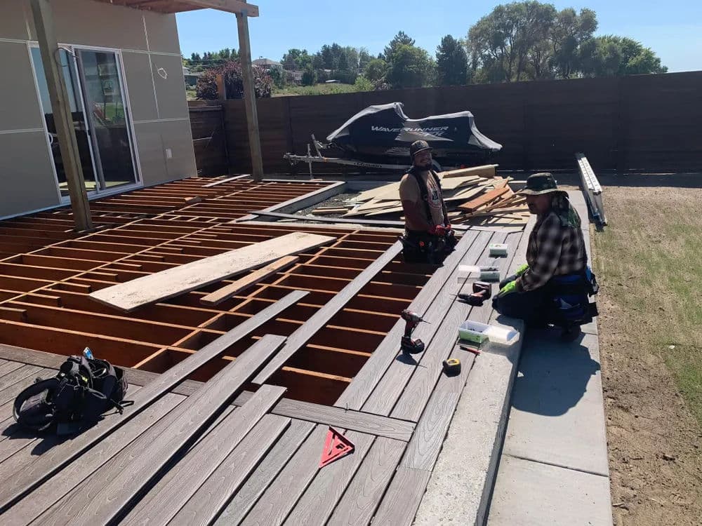 Two construction workers installing a wooden deck on a home with tools and materials.